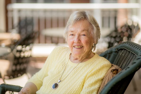 A smiling elderly woman sitting in a chair outdoors