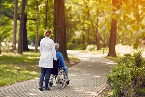 Caregiver assisting a resident in a wheelchair on a path