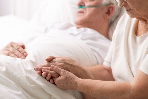A caregiver holding the hand of a resident in bed