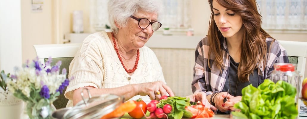 Senior resident and caregiver preparing fresh vegetables together