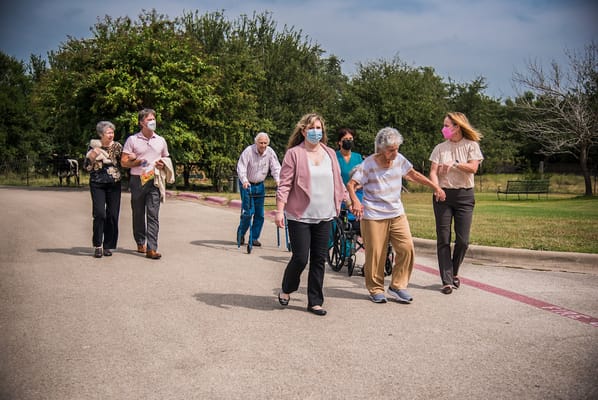 Residents and staff walking together outdoors in a garden area.