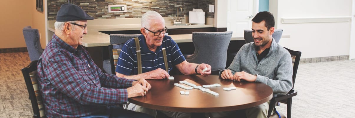 Residents playing dominoes with staff in an activity room