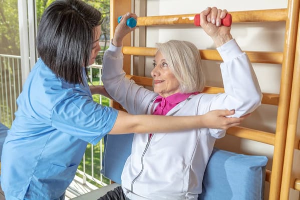 Staff assisting a resident with weights in a bright activity room