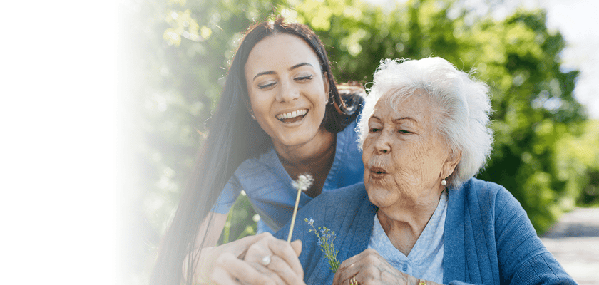 A caregiver interacting with a smiling elderly woman outdoors