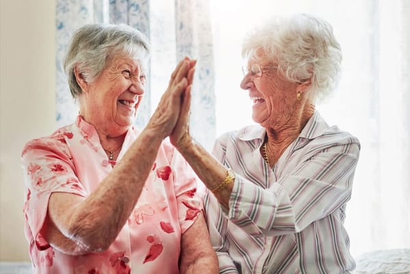 Two elderly women laughing and giving a high five