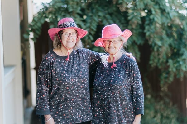Two residents smiling outdoors wearing matching pink hats