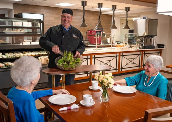Chef serving a salad to two residents at a dining table