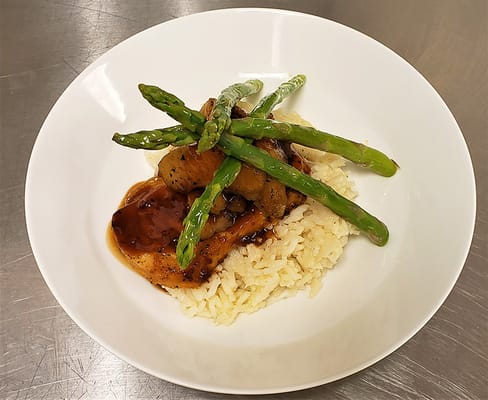 A plated meal featuring chicken, rice, and asparagus