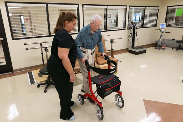 Staff assisting a resident with a walker in a therapy room