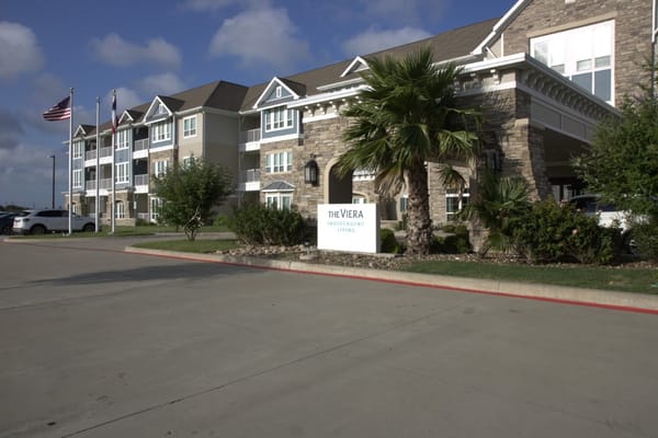 Front view of The Viera Senior Living facility with palm trees and American flags