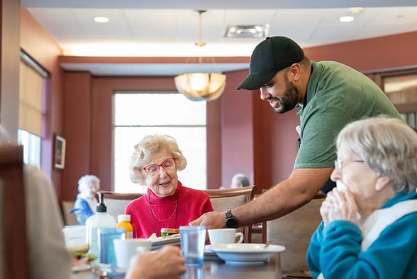 Residents enjoying a meal in the dining room with staff assistance