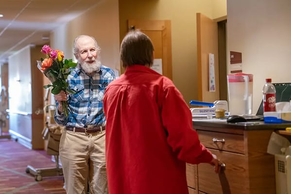 An elderly man holding flowers in a hallway.