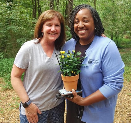 Two staff members smiling with a plant outdoors