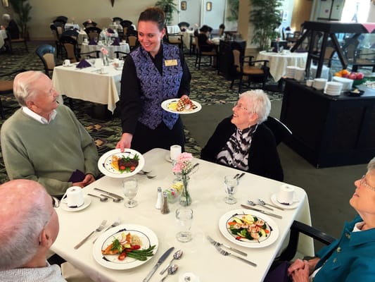 Dining room scene with residents and staff serving food