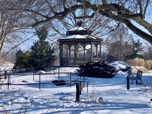 A winter scene featuring a gazebo in a snowy garden
