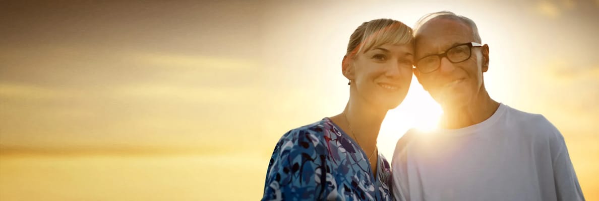 A senior man and a woman smiling outdoors with a sunset