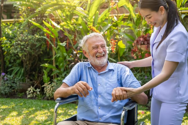 A caregiver assisting a smiling resident outdoors