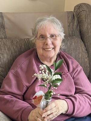 A smiling resident holding flowers in a cozy chair