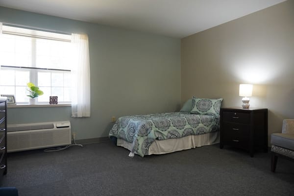 A clean, simple resident room with a bed and dresser.