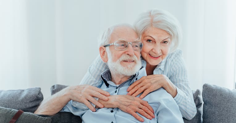 An elderly couple smiling together on a couch
