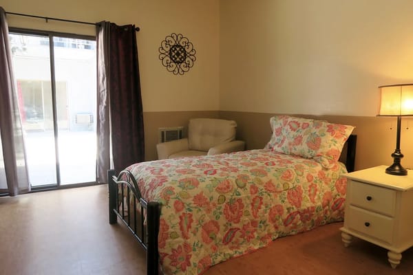 A bright and inviting bedroom with a colorful floral bedspread, chair, and lamp.