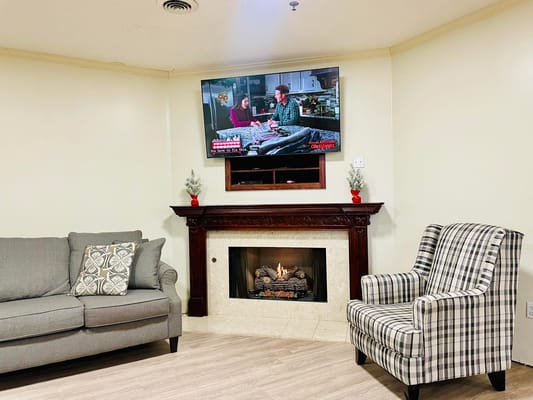 Living room with a gray sofa, plaid armchair, and a TV above a fireplace