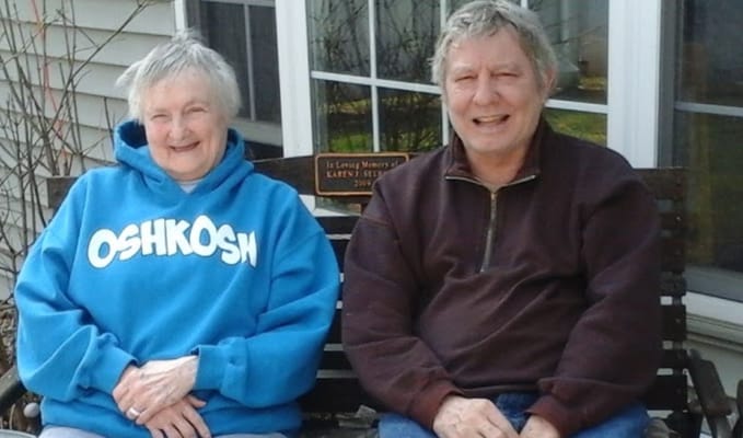 Two seniors sitting on a bench, smiling at the camera.
