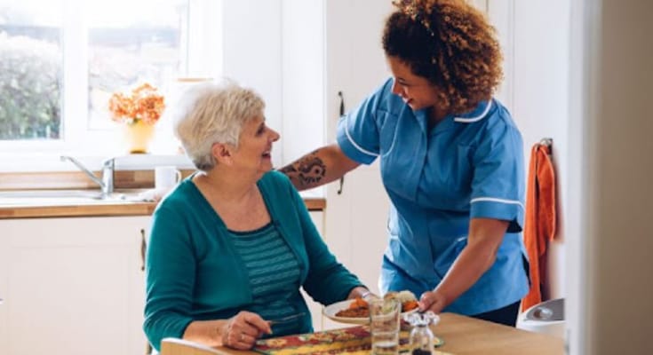 Caregiver serving meal to senior resident in kitchen