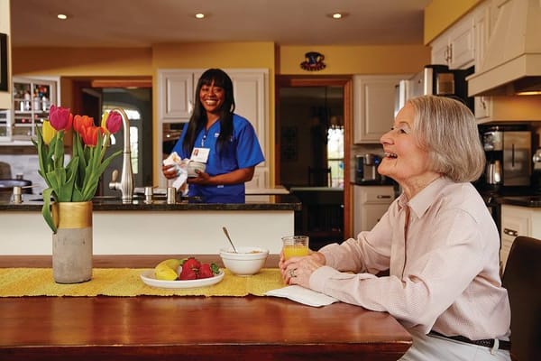 Resident enjoying breakfast with a caregiver in the kitchen