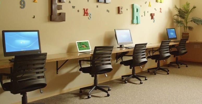 Empty computer lab with several sleek computers and rolling chairs