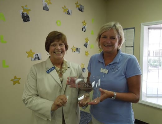 Two staff members holding an award in a decorated room