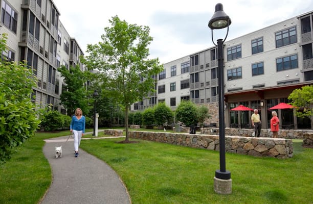 A woman walking a dog along a pathway, with other residents conversing nearby.