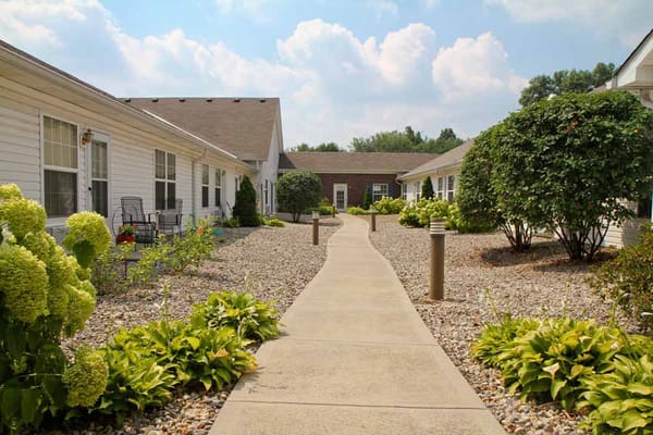 A landscaped pathway surrounded by greenery and buildings at a senior living facility.