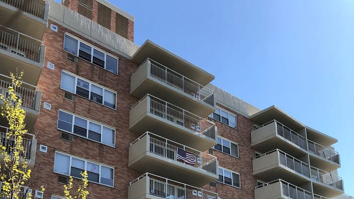 Exterior view of Fort Schuyler House with balconies and tree in foreground.
