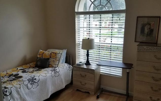 A well-furnished bedroom with a bed, lamp, and dresser in Gardens At Maplewood