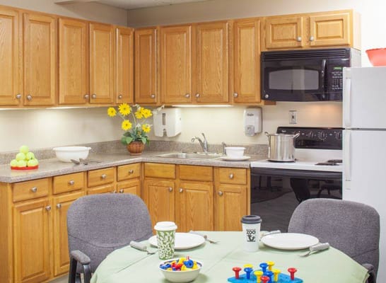 A cozy kitchen with wooden cabinets, a table set for dining, and bright flowers.
