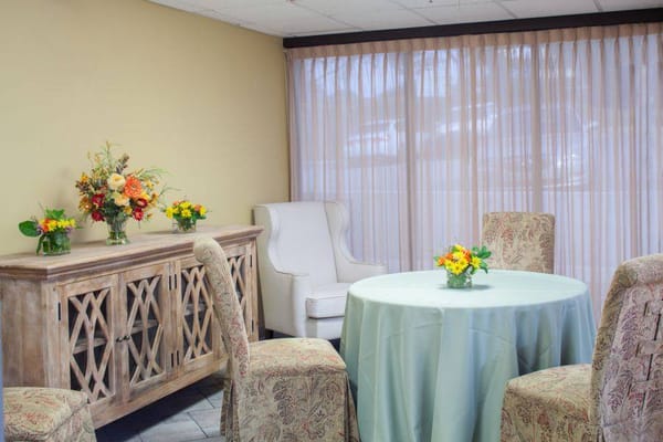 A cozy common area with a table, chairs, and floral arrangements.