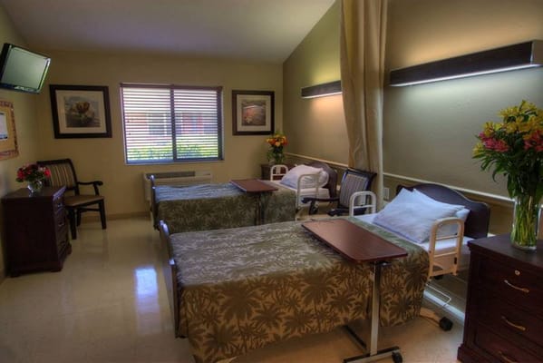 Bright shared room with two adjustable beds and flowers.
