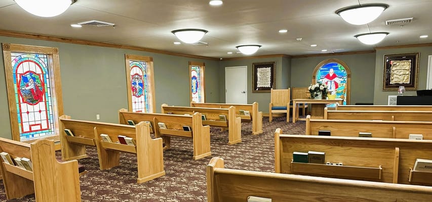 Interior view of a chapel with wooden benches and stained glass windows