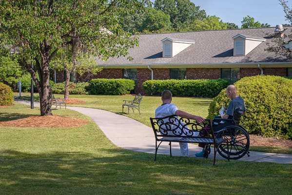 Two men sitting on benches in a garden area of a senior living facility