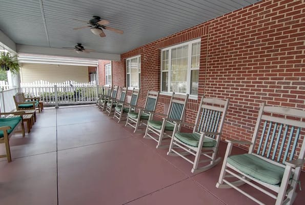 A porch featuring several rocking chairs and a view of the garden.