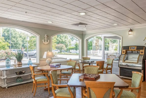 Brightly lit lounge area with tables and chairs, featuring large windows and a jukebox.