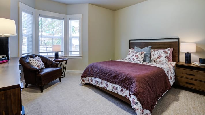 A well-furnished bedroom with a bed, chair, and window light.