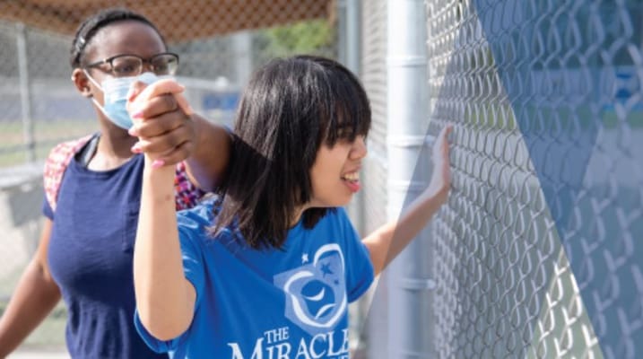 Two individuals participating in an outdoor activity near a fence.