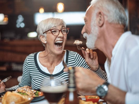 Two seniors sharing a joyful meal together, laughing.