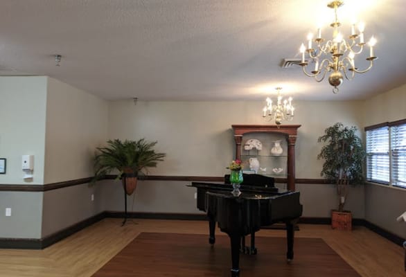 A well-lit common area with a piano and decorative plants