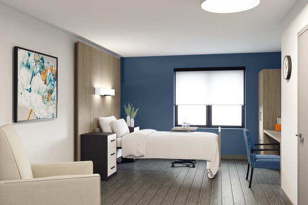 Resident room with bed, desk, and seating area in a senior living facility