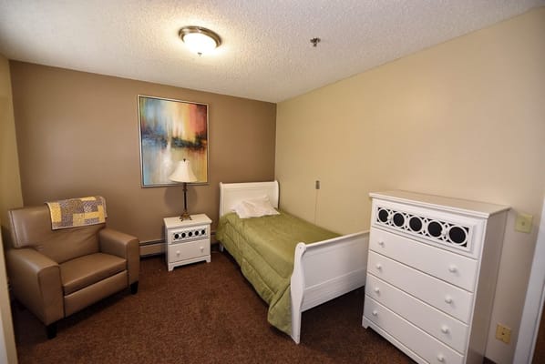 A cozy bedroom featuring a bed, nightstand, armchair, and dresser.