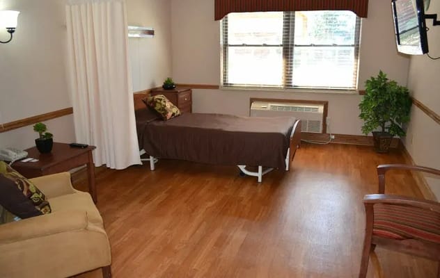 Interior of a senior living room with a bed, chair, and dresser.