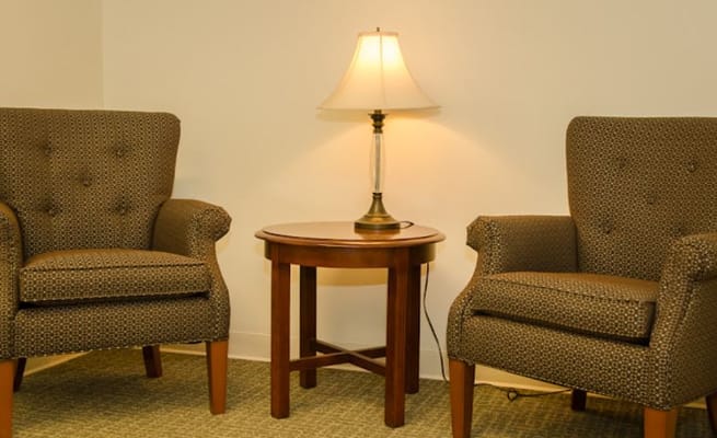 Two upholstered armchairs and a lamp beside a wooden side table